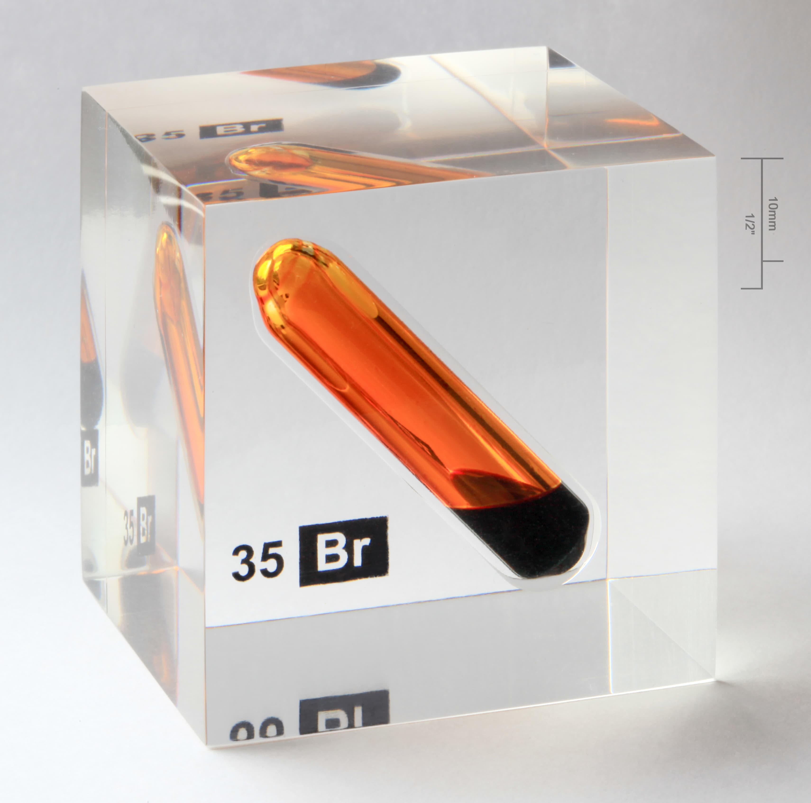 A sealed vial of red-brown bromine liquid inside a clear acrylic cube.