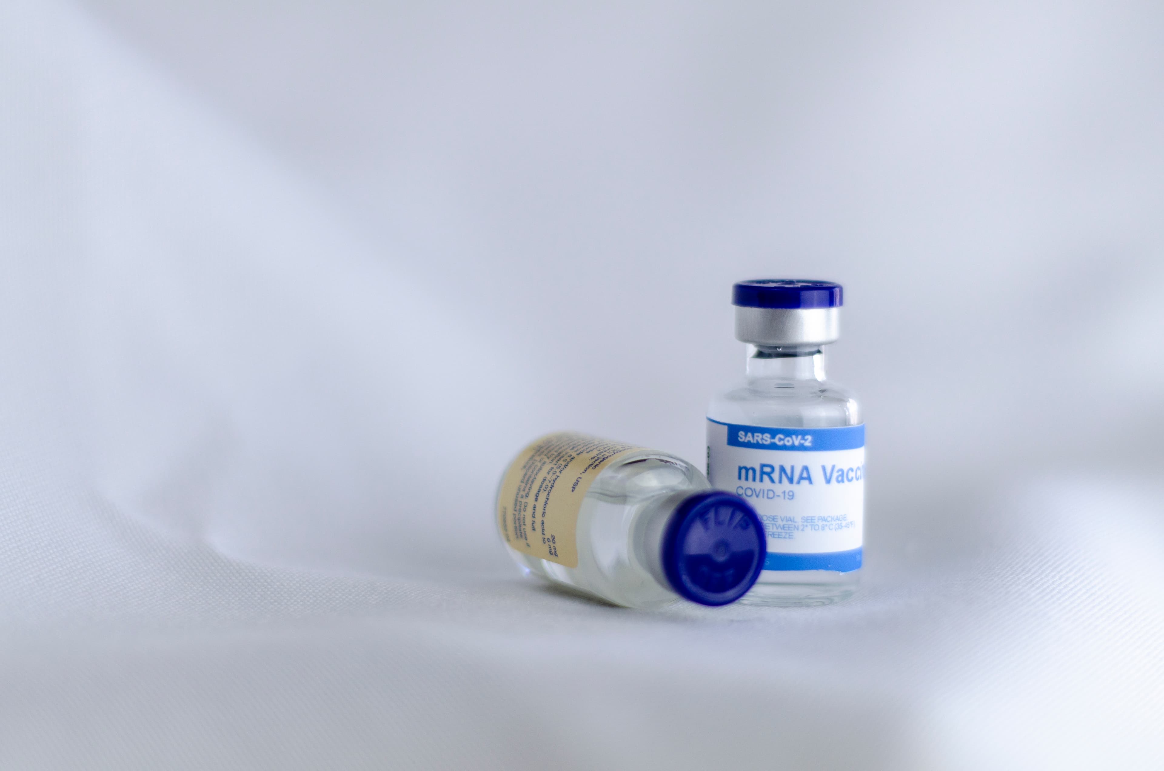 A small vial labeled as an mRNA COVID-19 vaccine prop on a neutral background.